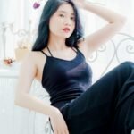 Stylish woman posing indoors on a decorative chair holding a flower, exuding elegance and grace.